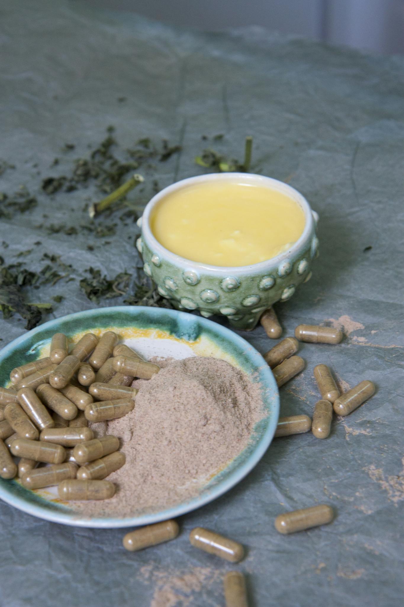 Close-up of herbal capsules, powder, and yellow cream on decorative plates.